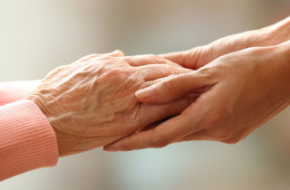 一位临终关怀志愿者牵着一位老妇人的手。
