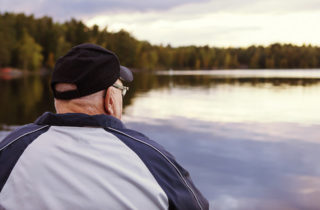 senior man contemplating while staring at a lake outside
