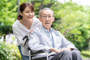 Young woman with grandfather in wheelchair in park.