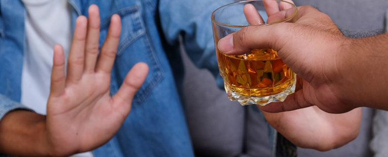 person saying no to friend offering glass of whiskey
