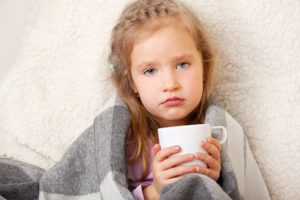 发烧的年轻女孩披着毯子，喝着热茶