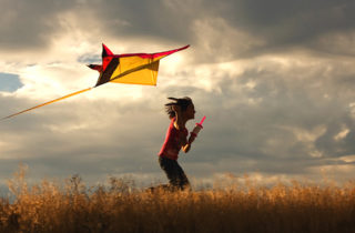 Young girl running in wheat field with kite under cloudy skies