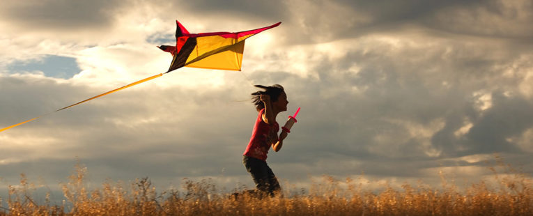 年轻的女孩在小麦田里跑着风筝，在云彩下的天空下