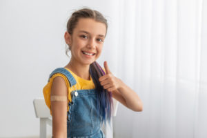 小女孩在接种疫苗后，手臂上缠着绷带竖起大拇指。