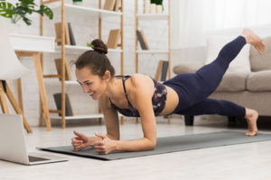 Woman exercising while watching instructional video on laptop.