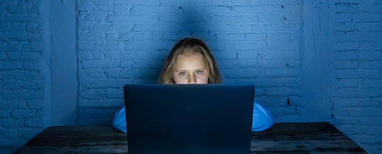 Young girl on a computer in a dark room doing online learning.