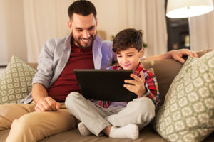 Father and son using a tablet on a couch.