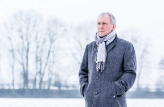senior man stands solemnly outside in a coat and scarf during winter