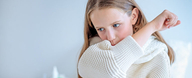 Girl in white sweater coughs into elbow