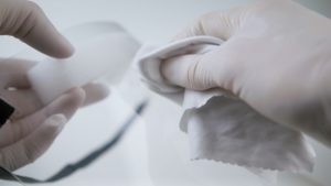 two latex gloves hands clean a face shield with wipes