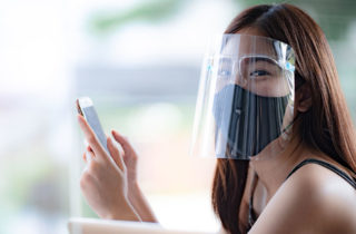 girl wearing a mask and a faceshield reads her cellphone