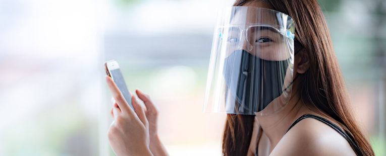 girl wearing a mask and a faceshield reads her cellphone