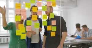 two women and a man stand in from of a glass wall full of post-it's collaborating on ideas
