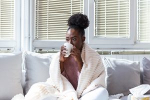 woman on a couch drinks from a mug wrapped in a blanket