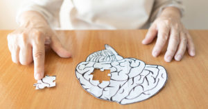 老妇人用手把缺失的白色拼图片放进人脑形状的地方。创造性的想法，记忆丧失，痴呆，阿尔茨海默病和心理健康的概念。