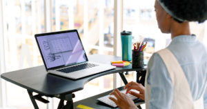 woman stands working on a laptop with the use of a standing desk