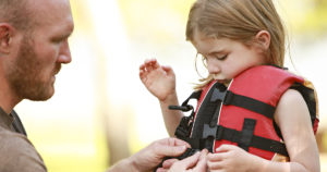 father helping daughter with life jacket
