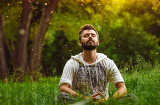 Man practicing progressive muscle relaxation sitting in a field with eyes closed