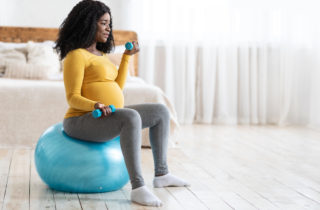 一名孕妇坐在健身球上，手持重物，在怀孕期间安全地锻炼。