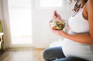 A pregnant woman eats a salad while learning about what to eat during pregnancy.
